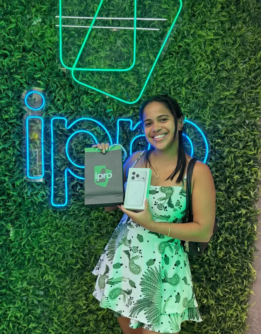 Cliente da iPro com o iPhone novo em frente à parede de neon da loja